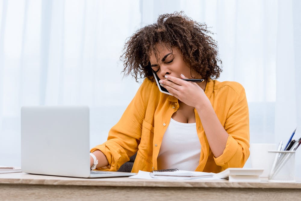 woman yawning on phone and laptop