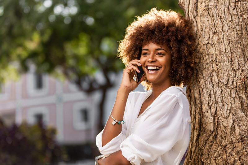 woman leaning against tree talking on phone